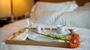 a bed with a white coverlet and a breakfast tray with an orange flower, white plate and white coffee cup